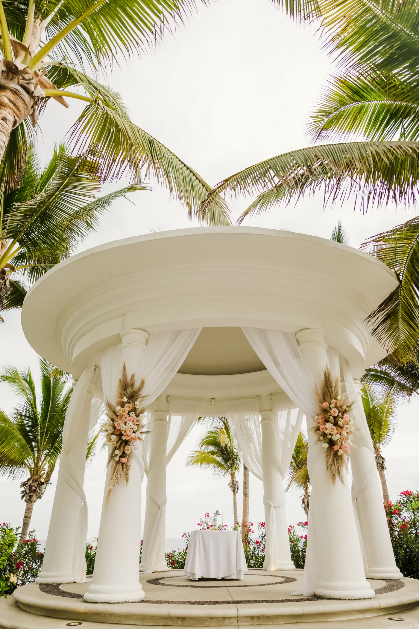 White gazebo decorated with pink flowers and pampas grass for a beach wedding