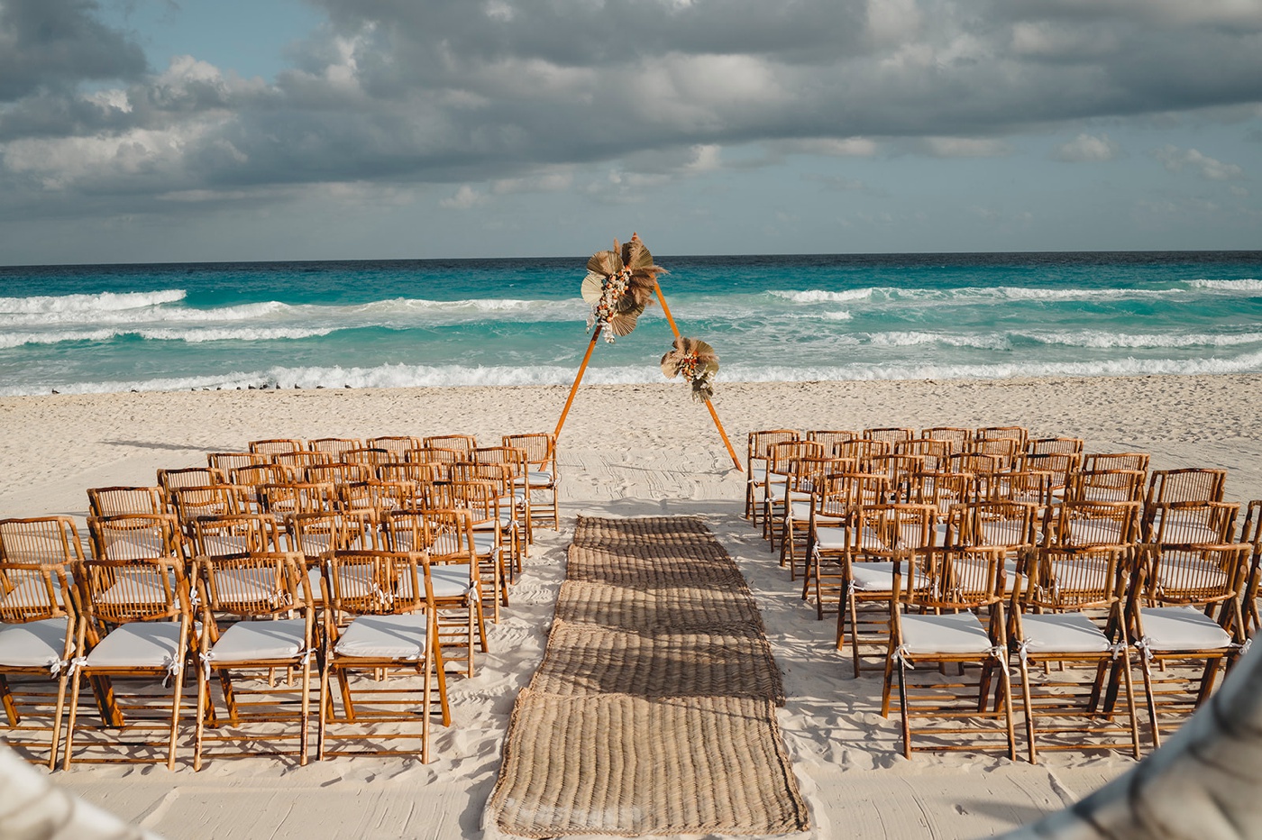 Beach wedding ceremony with a thatched aisle runner and triangle arch