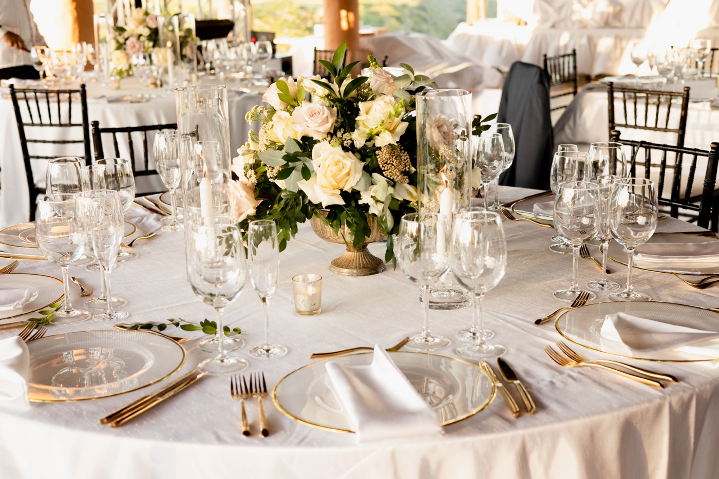 Wedding reception table with white linens, gold cutlery, and a gold bud vase filled with pink and white flowers