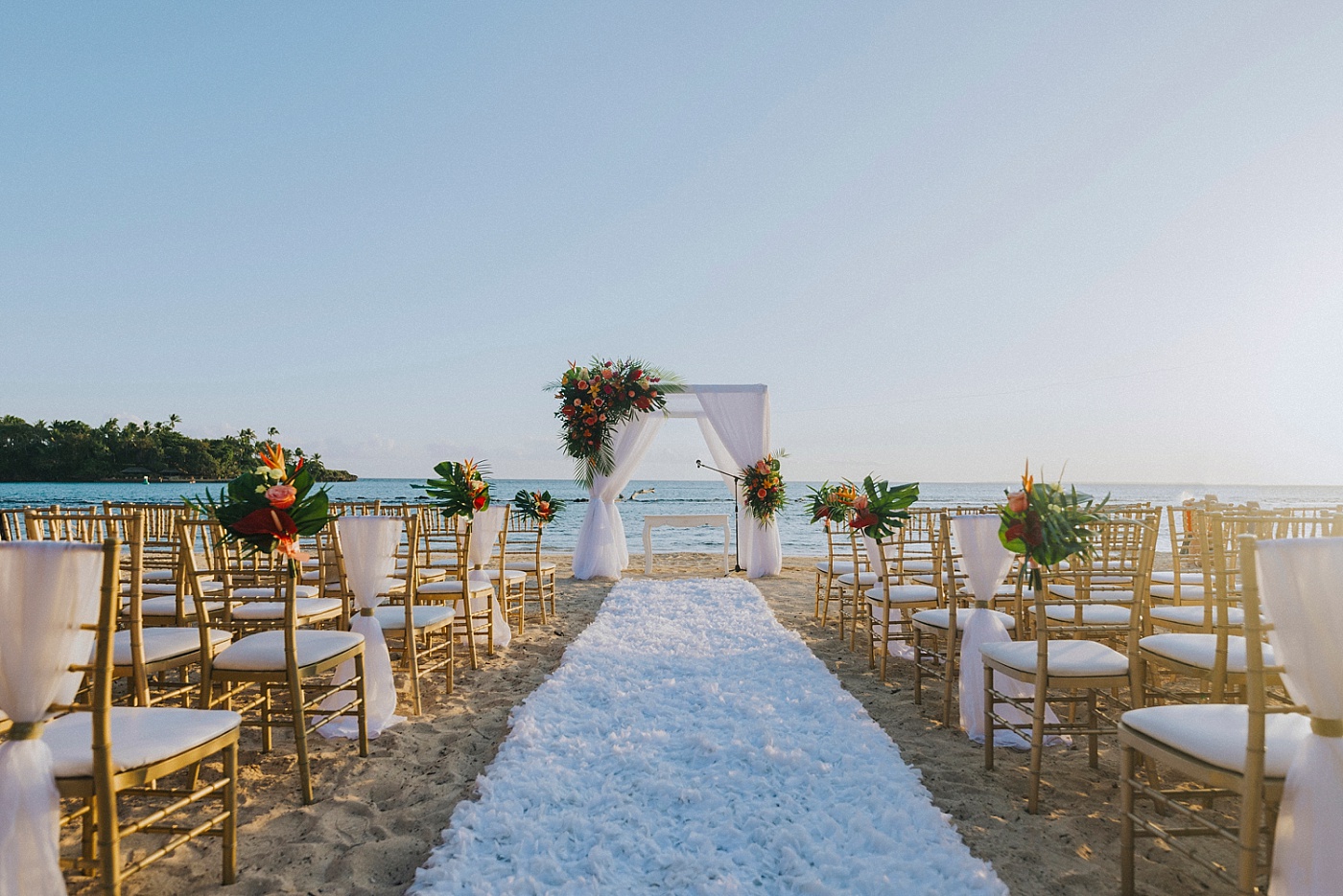 Wide shot of beachside ceremony location at Casa de Campo with gold chairs and a Chuppah