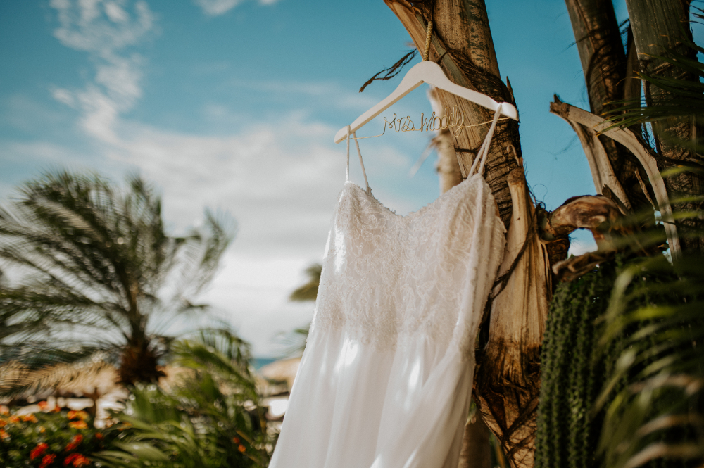 Bride’s wedding dress hanging on palm tree at beach resort, reflecting destination wedding cost and tropical setting