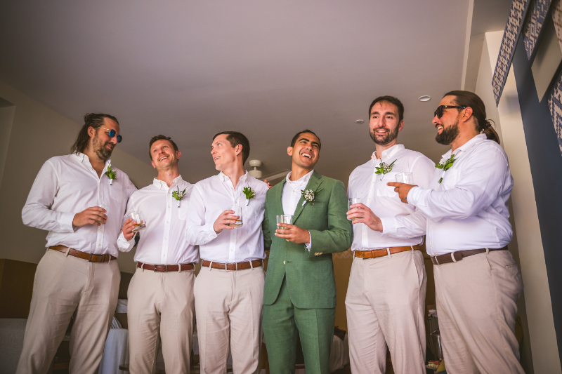 Groomsmen getting ready, laughing with drinks, destination wedding pros and cons group prep moment