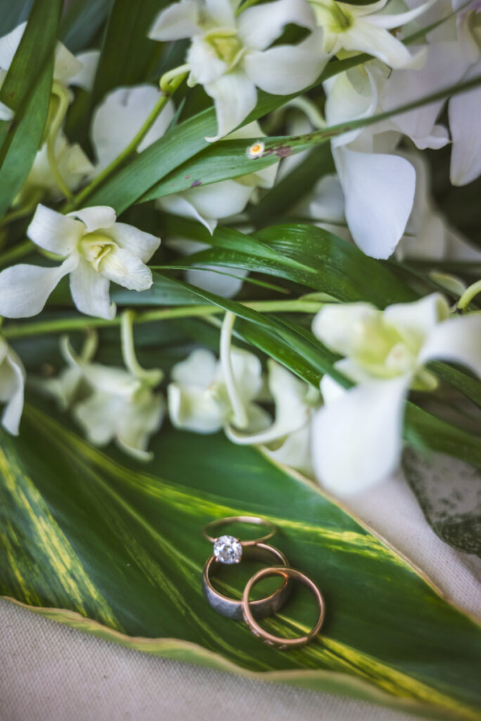 Wedding rings on tropical leaf with white flowers, destination wedding pros and cons romantic detail shot
