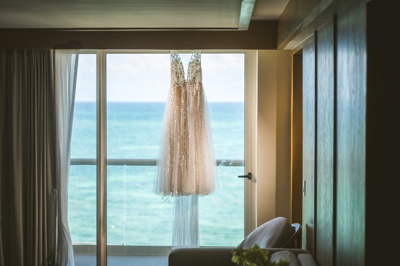 Wedding dress hanging by ocean view balcony, destination wedding pros and cons bridal prep moment
