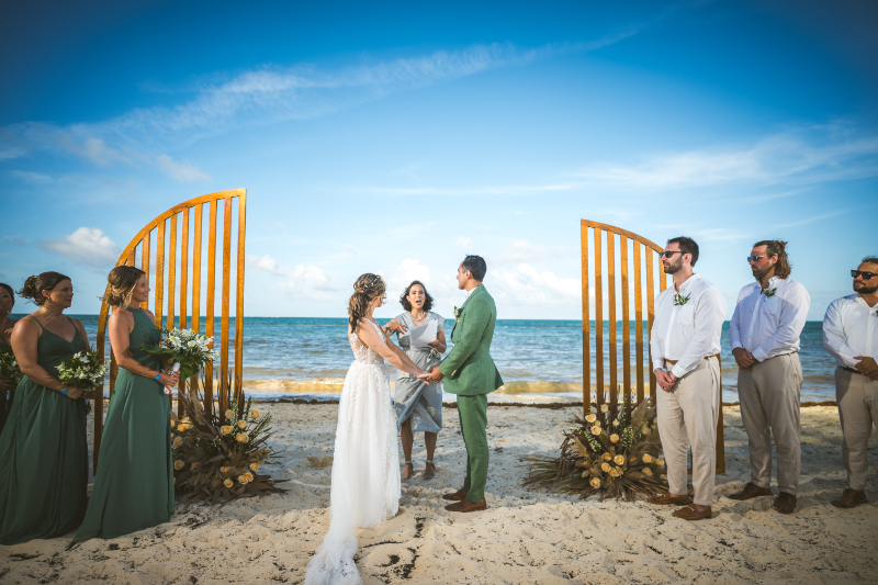 Couple exchanging vows on beach with wedding party standing beside them