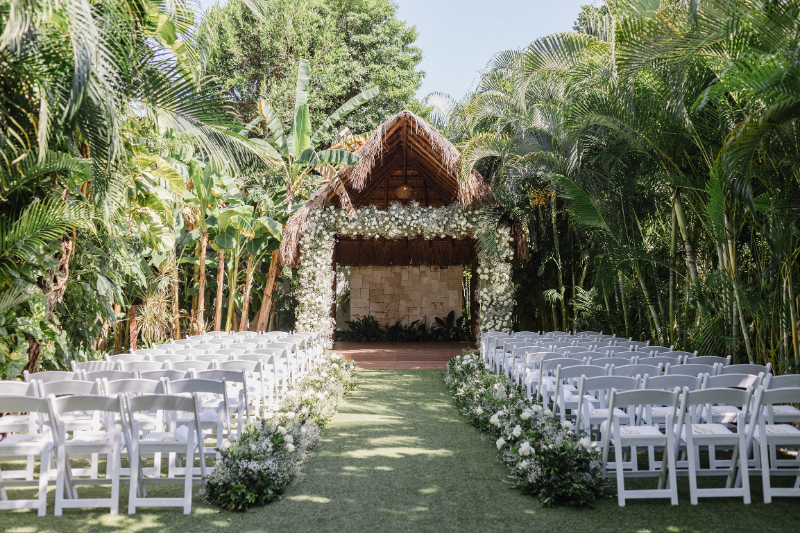 Just engaged destination wedding ceremony setup with tropical greenery, floral arch, and elegant outdoor seating arrangement