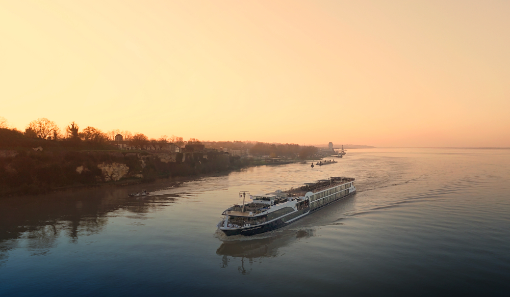 Luxury river cruise ship sailing at sunset along calm river with scenic shoreline and soft golden light