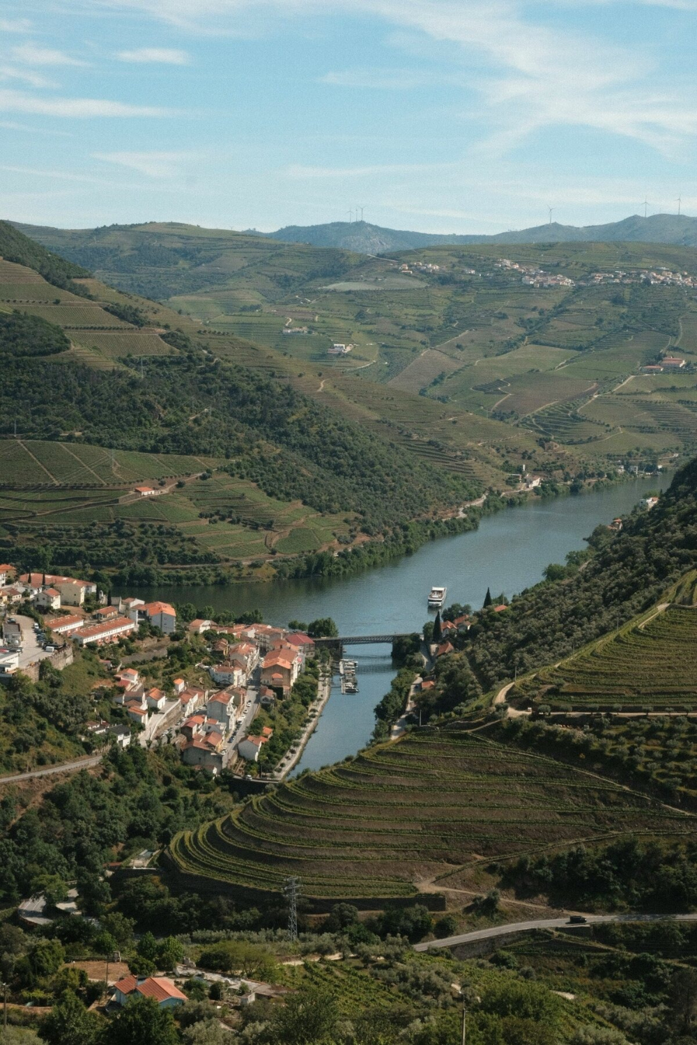 Scenic river winding through hillside vineyards and small village with bridge and boat in valley view