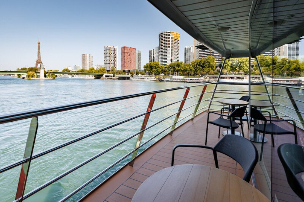 Luxury river cruise deck with seating overlooking river and Paris skyline, including Eiffel Tower views