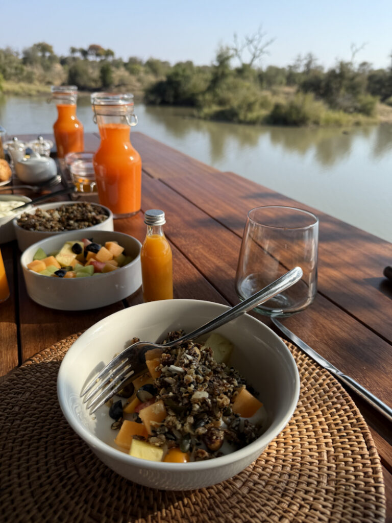 Safari lodge breakfast with fresh fruit and juice by water, included in African safari cost experience