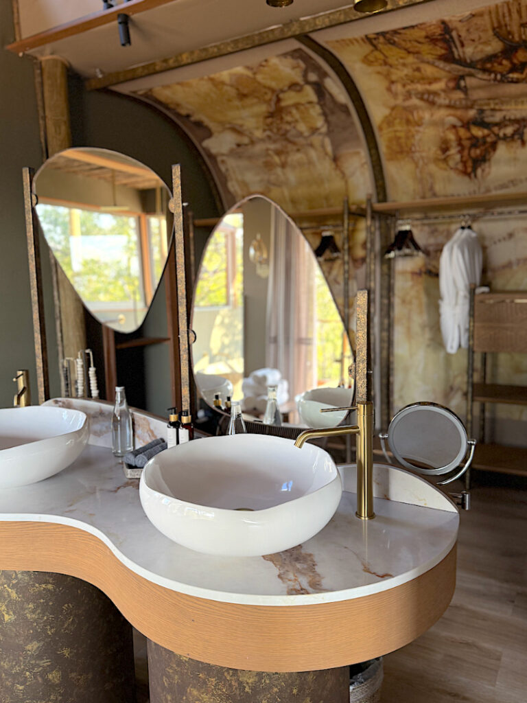 Luxury safari lodge bathroom with double vanity, marble finishes, and natural light overlooking private deck