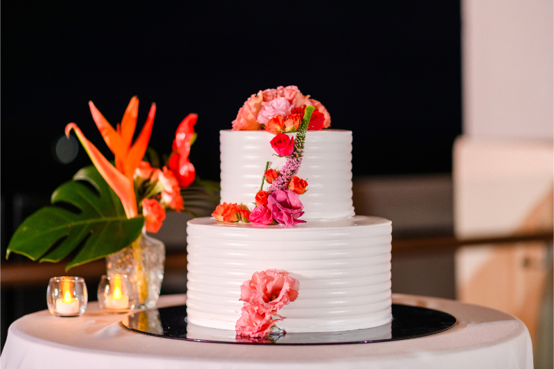 Two-tier white wedding cake with tropical flowers and romantic candlelit reception décor.