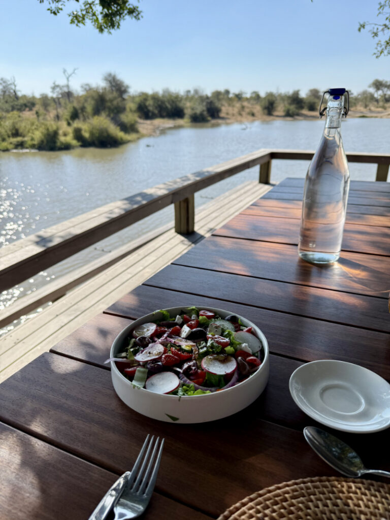 Fresh salad served on a wooden deck overlooking water, with soft light and a relaxed outdoor dining setting