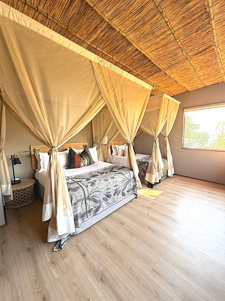 Luxury safari-style lodge bedroom with canopy beds, warm neutral tones, and relaxing natural light.