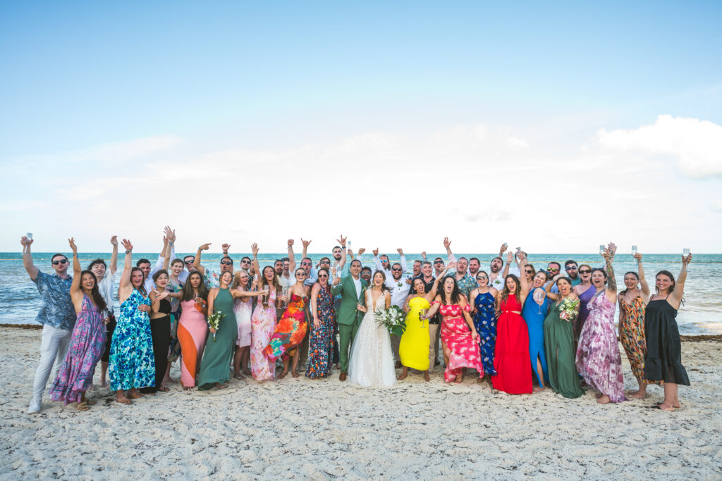 Wedding guests posing with bride & groom on the beach for a destination wedding at Royalton Splash Riviera Cancun.